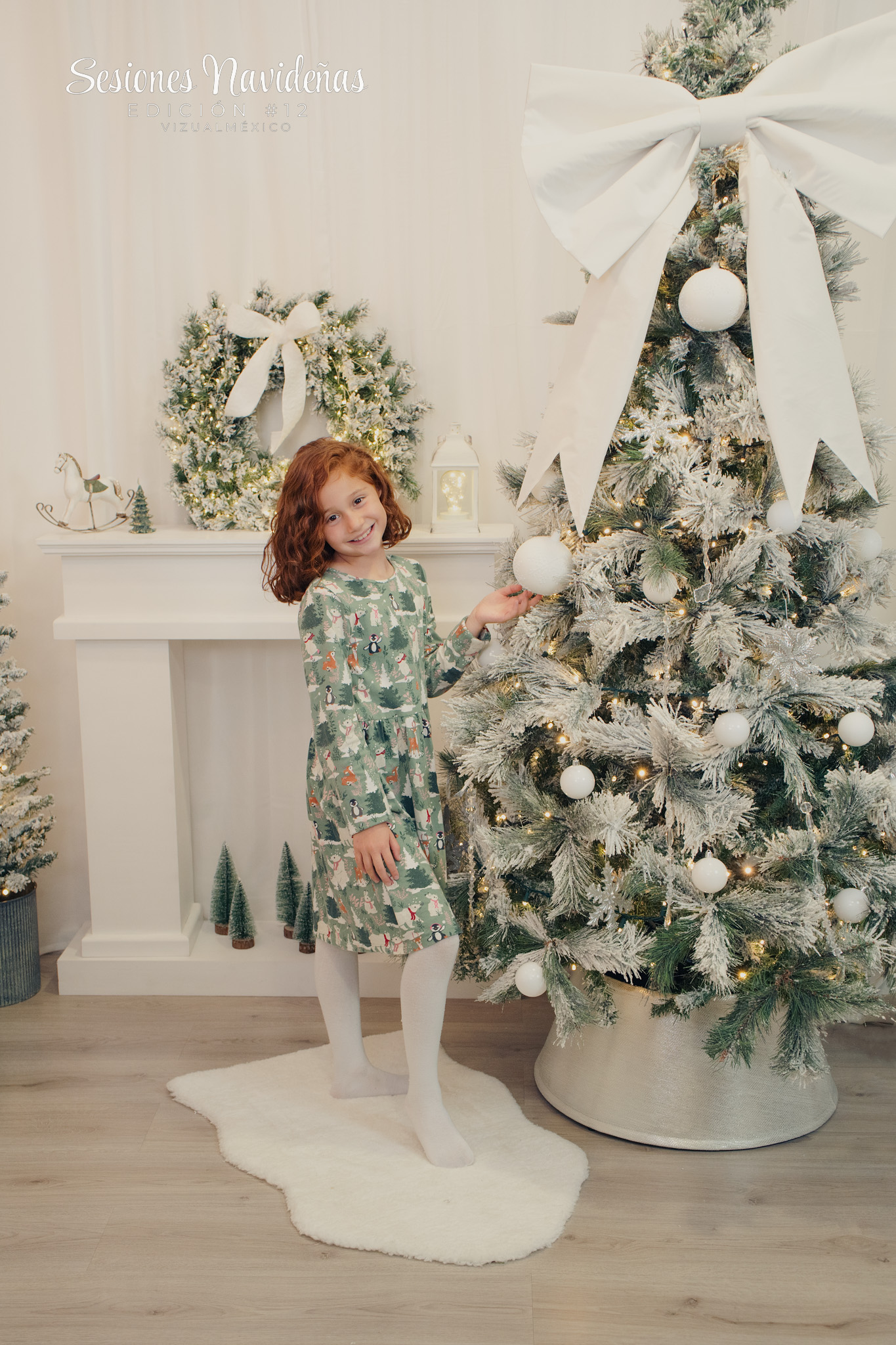 Foto de hermosa niña parada al lado de un árbol navideño decorado con moño blanco
